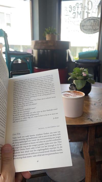 Coffee Circus Porto: Round wooden table with a cup of cappuccino and a small potted plant, with a book held open in the foreground.
