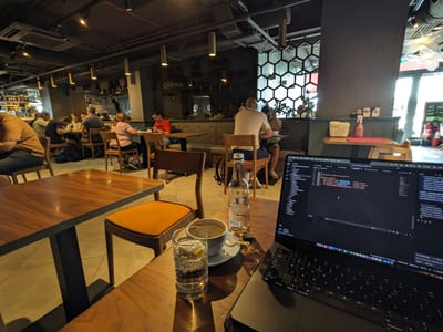 Busy Bee Cafe Sliema: Wooden tables with wooden chairs, one with a padded seat, a laptop and drinks on a table, several people seated and working or chatting.
