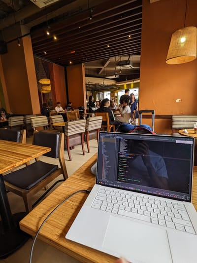 Highlands Coffee: Wooden tables with padded and wooden chairs, a laptop on one table, and several people seated and working or chatting inside the cafe.