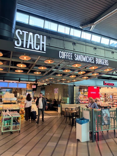 Stach Coffee: Large illuminated signs above the entrance read 'STACH' and 'COFFEE SANDWICHES BURGERS' with hanging lights and seating visible inside.