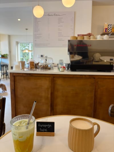 Louis Louis Espresso Bar: Round white table with a cold drink in a glass, a hot drink in a brown mug, and a small sign reading 'laptopvrije tafel'.