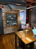 Wooden table with a small gold lamp and a chair beside a brick wall with a framed chalkboard sign about event space and co-work.