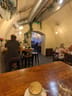 Mango's cafe: Long wooden table with an empty coffee cup and glass of water in the foreground, high stools at a counter and seated people in an arched room.