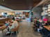 Starbucks: Two groups seated at wooden tables with padded chairs, some using laptops, with a long counter and menu screens in the background.