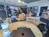 Starbucks: Round wooden tables with wooden chairs and a pair of cushioned armchairs around small tables, a retail display, and people ordering at the counter.