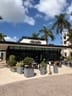 Narrative Coffee Roasters: Outdoor seating with black metal chairs and tables, separated from walkway by tall planters, in front of a glass-front coffee shop with a sign above.