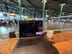 Wooden counter table with a laptop and a coffee cup facing a spacious terminal area with people and flight information screens.