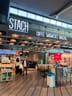 Stach Coffee: Large illuminated signs above the entrance read 'STACH' and 'COFFEE SANDWICHES BURGERS' with hanging lights and seating visible inside.